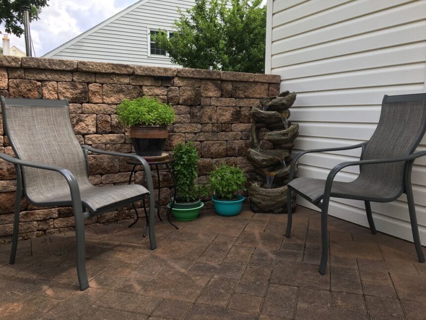 A patio with chairs and potted plants on the side.