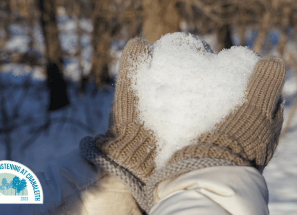 A person wearing mittens holding snow in their hands.