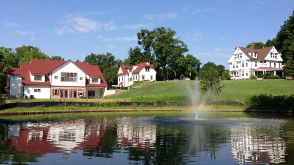 A photo taken from the pond, with the fountain on, and the historic house, administration building, and conference center in the distance.