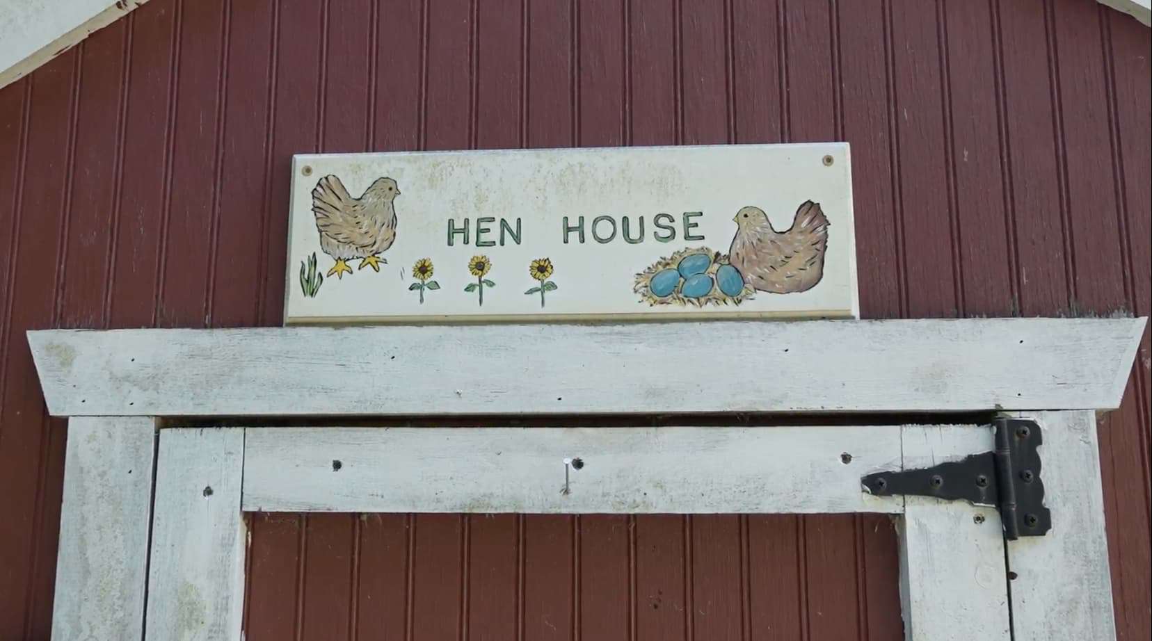 A red Hen House with a sign with painted chickens and flowers on it.