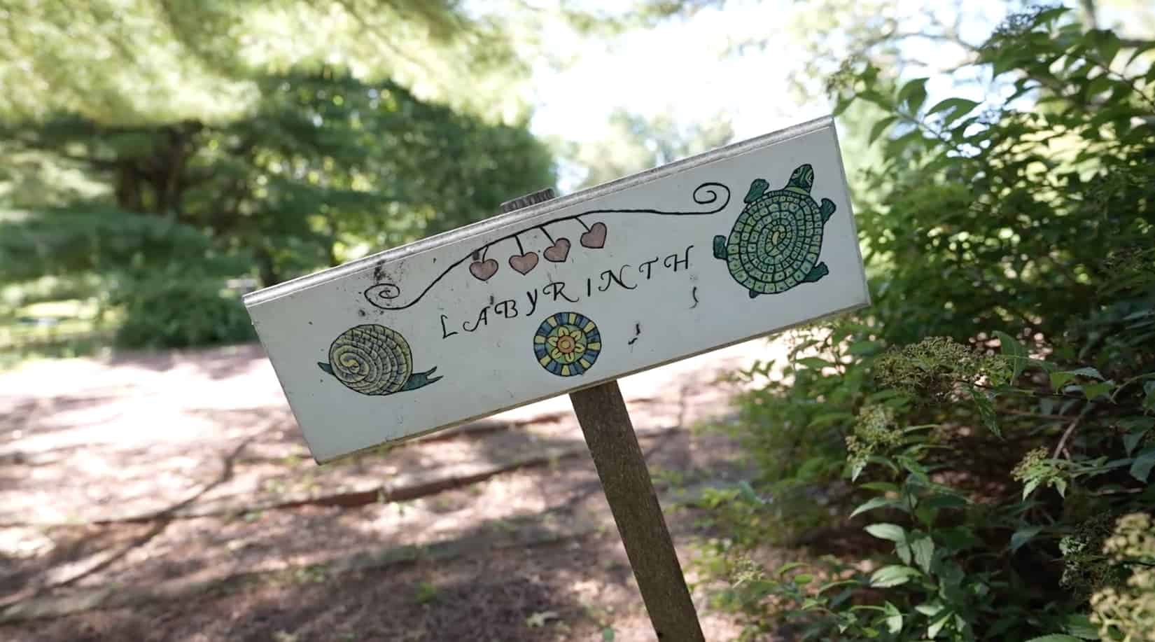 A white labyrinth sign, with hearts, a snail, and turtle.