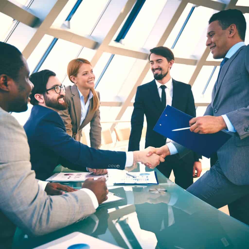 Five men and women in suits shaking hands while speaking about business.