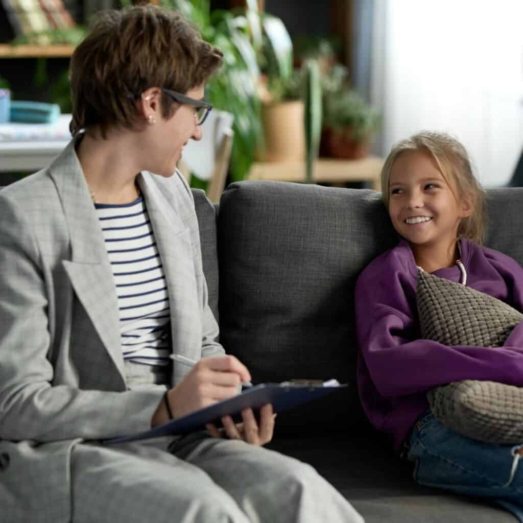 A Social worker writing while smiling with a happy kid holding a pillow.