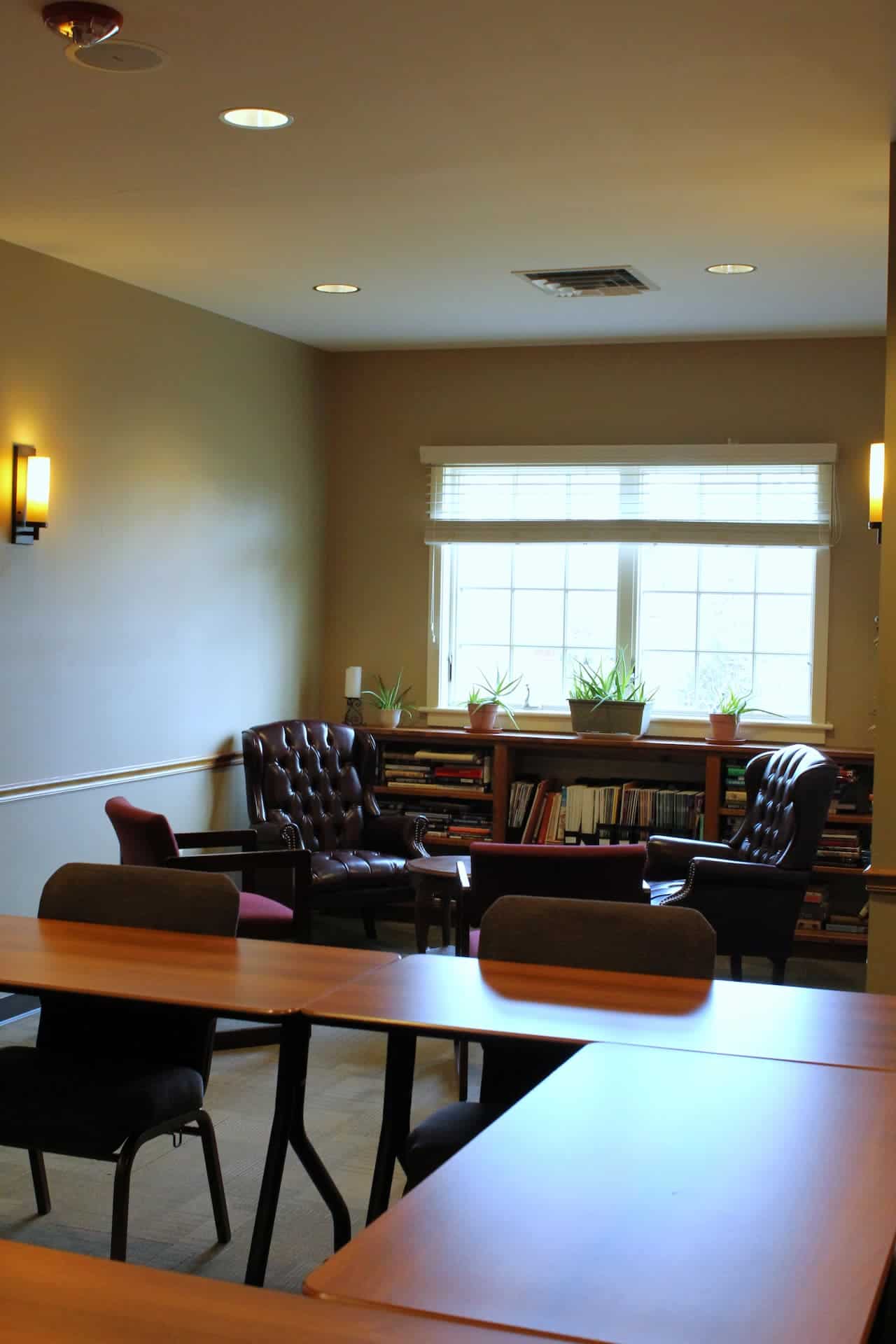 Board Room tables with two comfortable chairs by a bookcase and window.