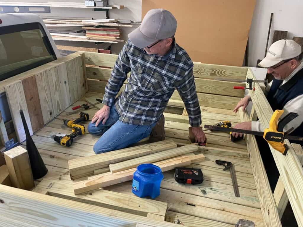 Two men working on a wooden truck bed.