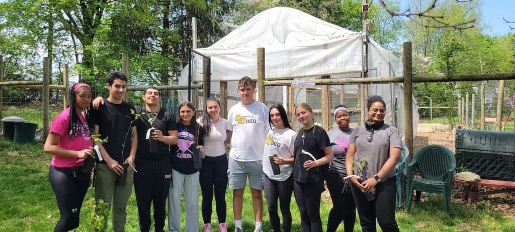 A group of young men and women standing in front of a garden posing for a photo.